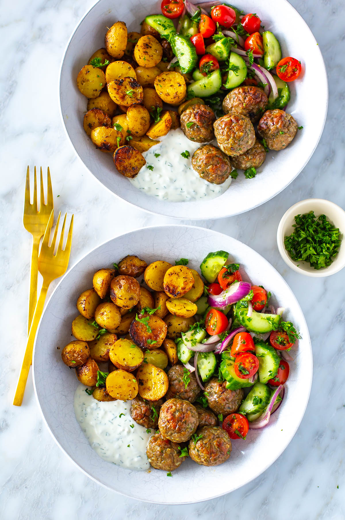 Two bowls of greek chicken meatballs with a side of potatoes, veggies and tzatziki.