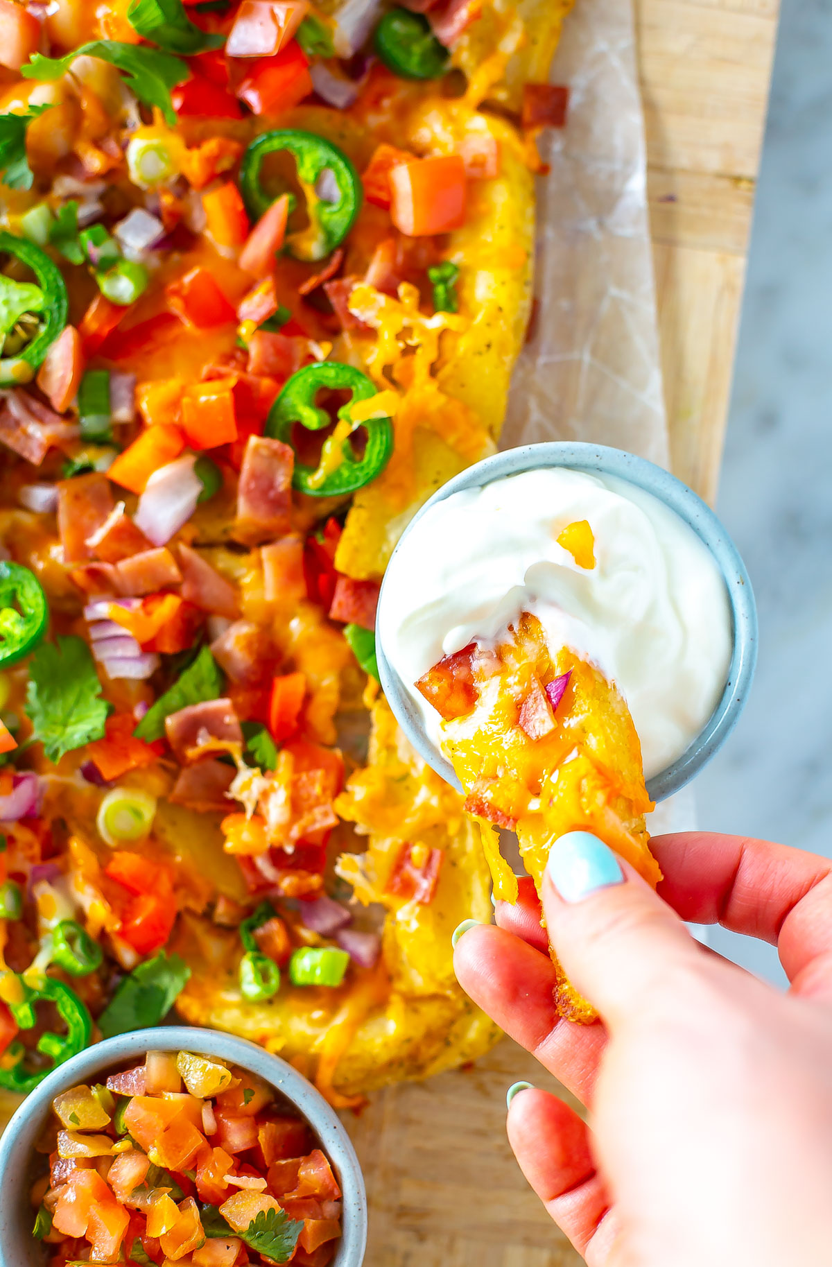 A close-up of someone picking up an Irish nacho and dipping it into sour cream.