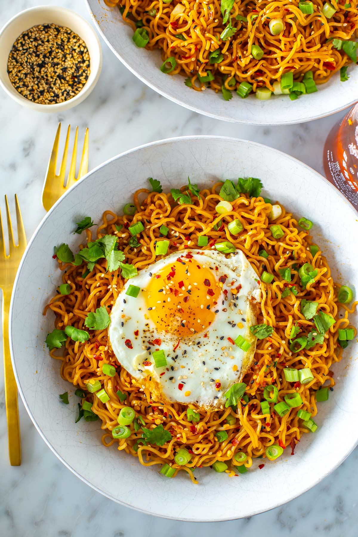 A bowl of spicy noodles topped with a fried egg, green onions and cilantro.