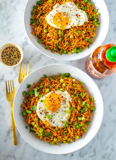 Two bowls of spicy noodles, each topped with a fried egg and green onions.