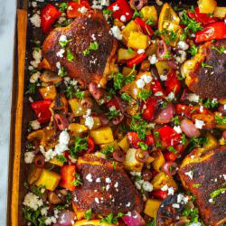 A close-up of baked chicken thighs on a sheet pan with vegetables.