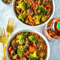 Two bowls of Instant Pot beef and broccoli with a bottle of sriracha on the side.