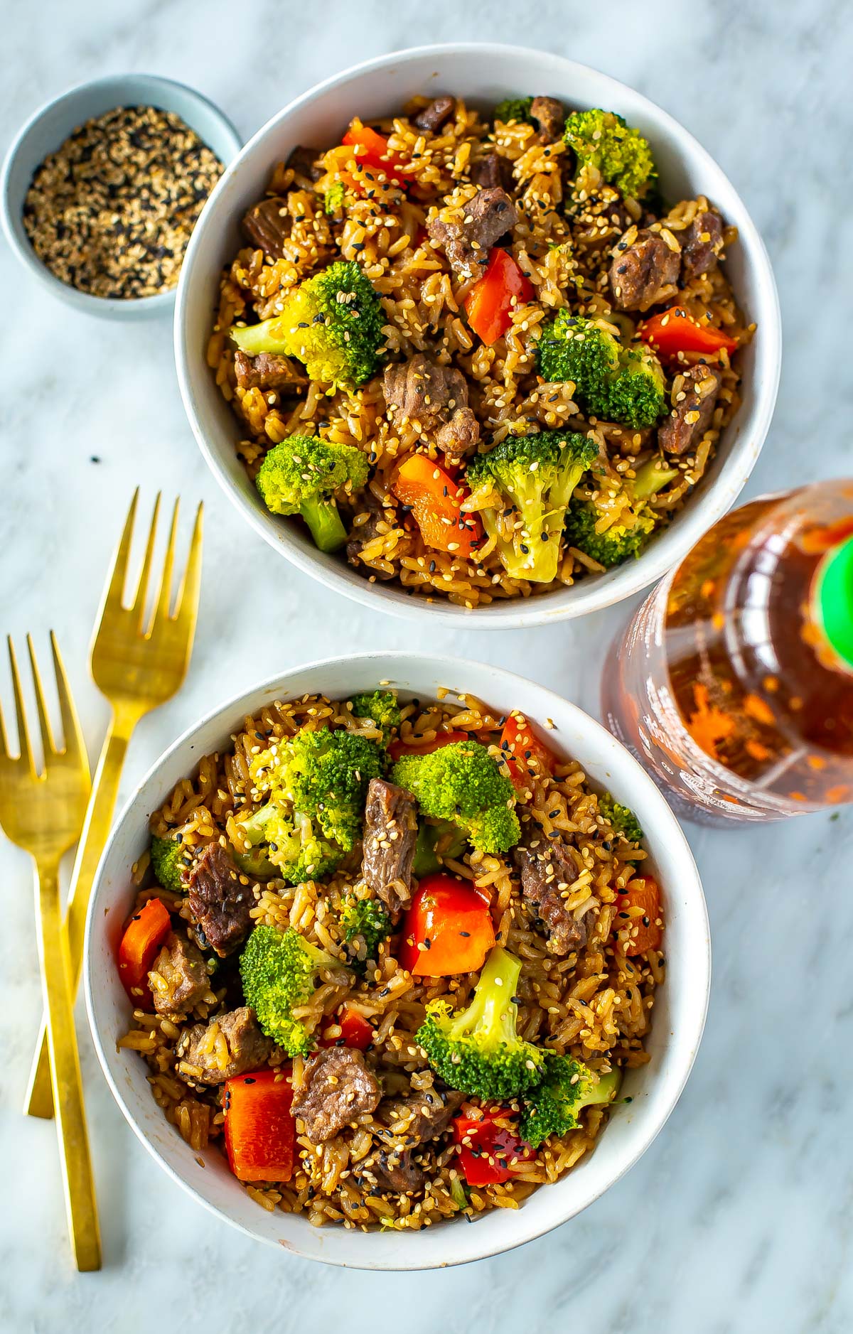Two bowls of Instant Pot beef and broccoli with a bottle of  sriracha on the side.