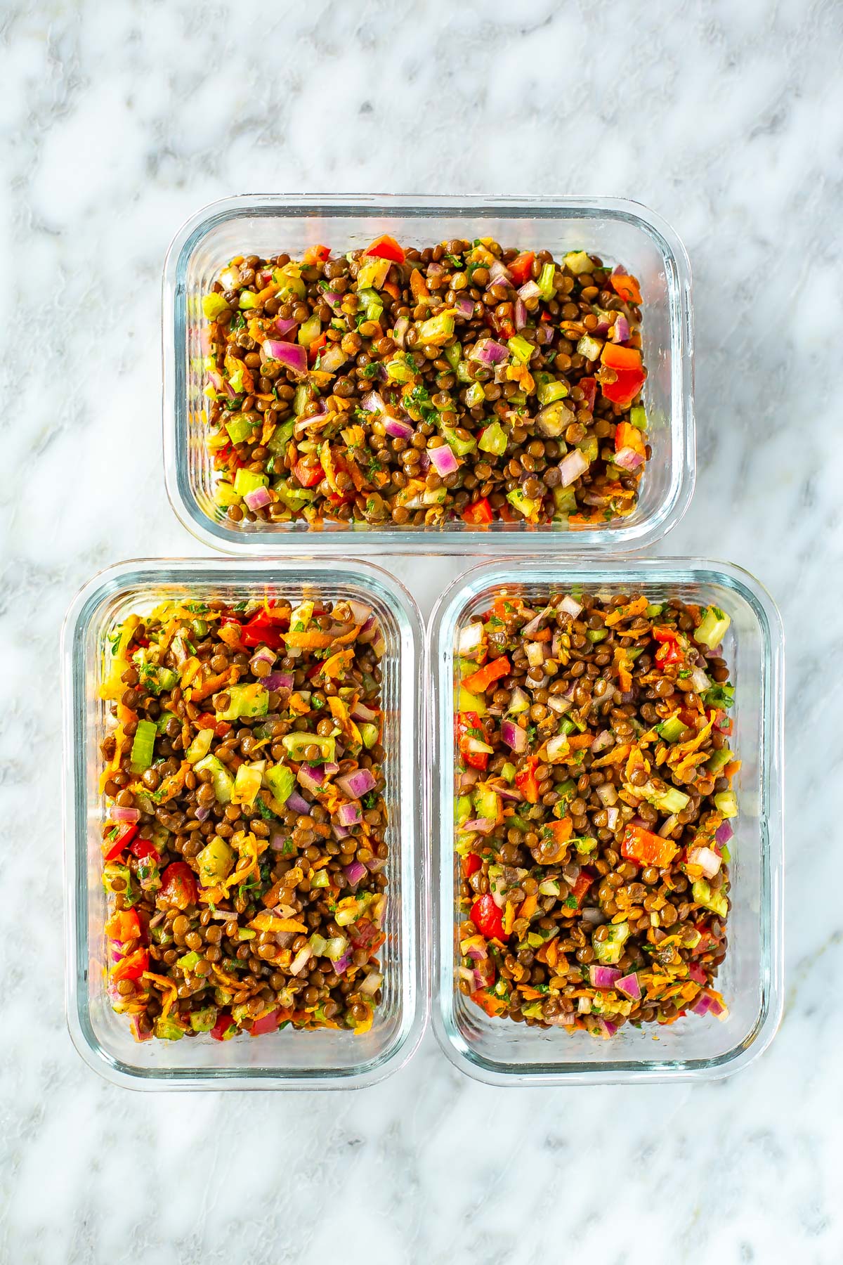 Three meal prep containers, each with a serving of lentil salad.