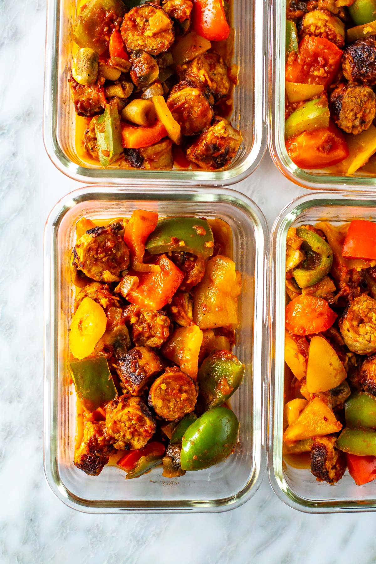A close-up of meal prep containers with sausage, peppers and onions.