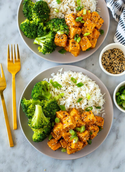 Two plates of air fryer tofu served alongside rice and broccoli.