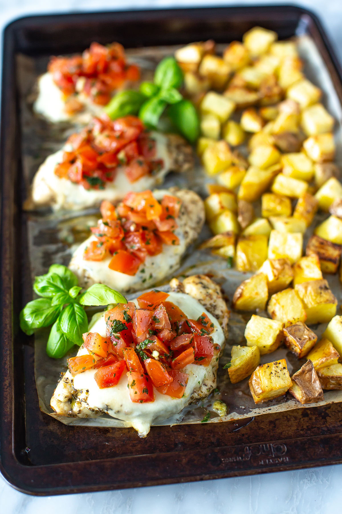 A sheet pan with chicken, potatoes and tomatoes