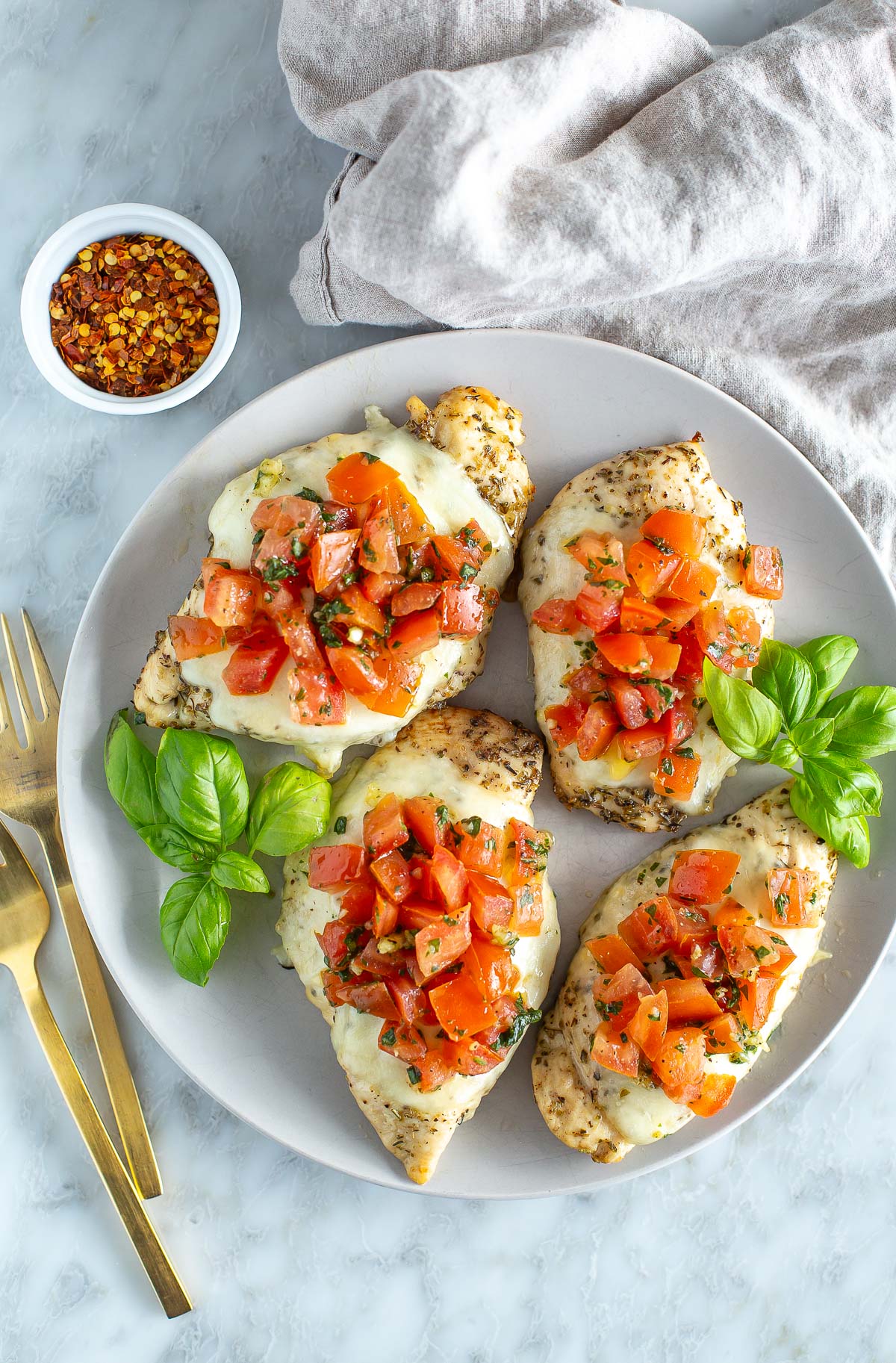 Three pieces of chicken with tomatoes and basil on a plate