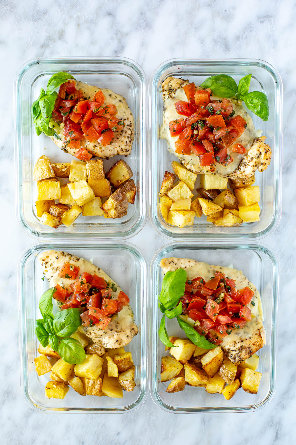 Four square containers with chicken, potatoes and bruschetta