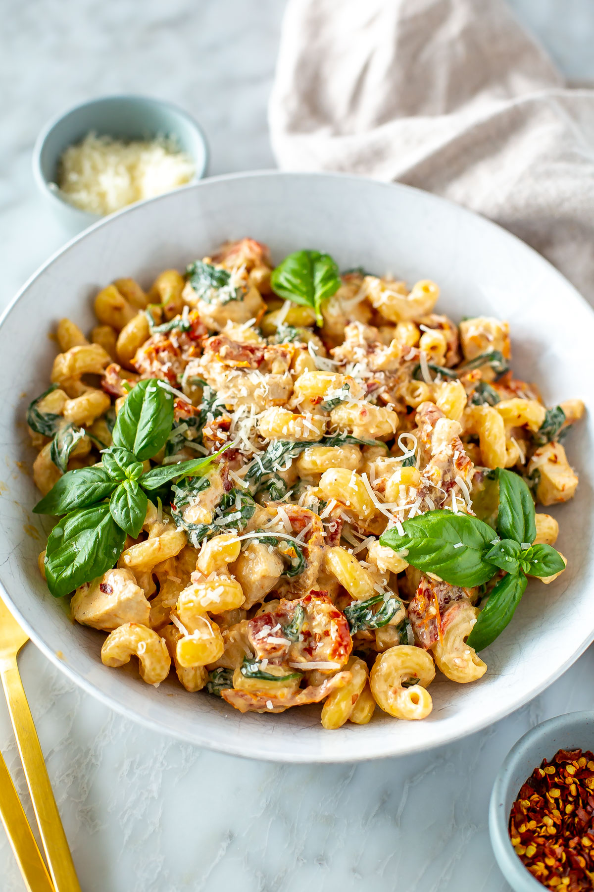 A bowl of creamy sundried tomato pasta with parmesan and red chili flakes on top.
