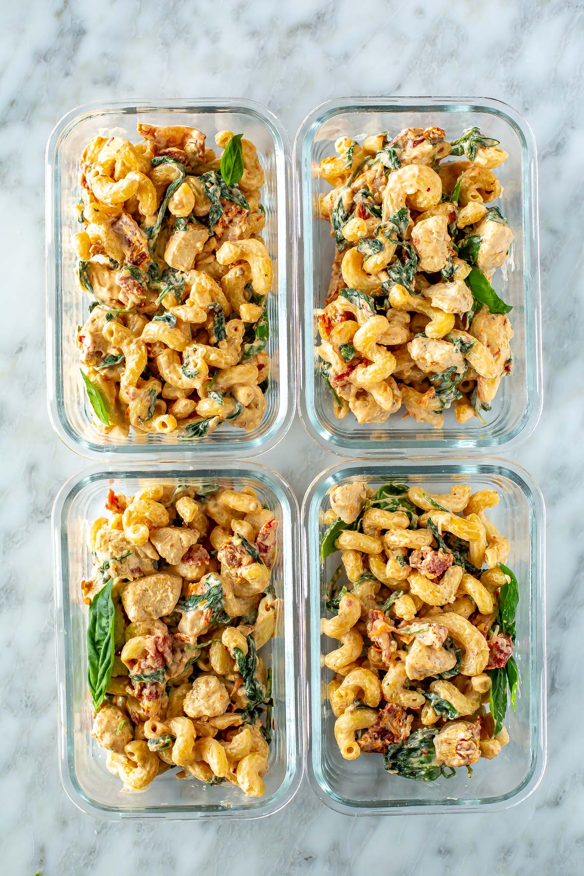 Four meal prep containers, each with a serving of creamy sundried tomato pasta.