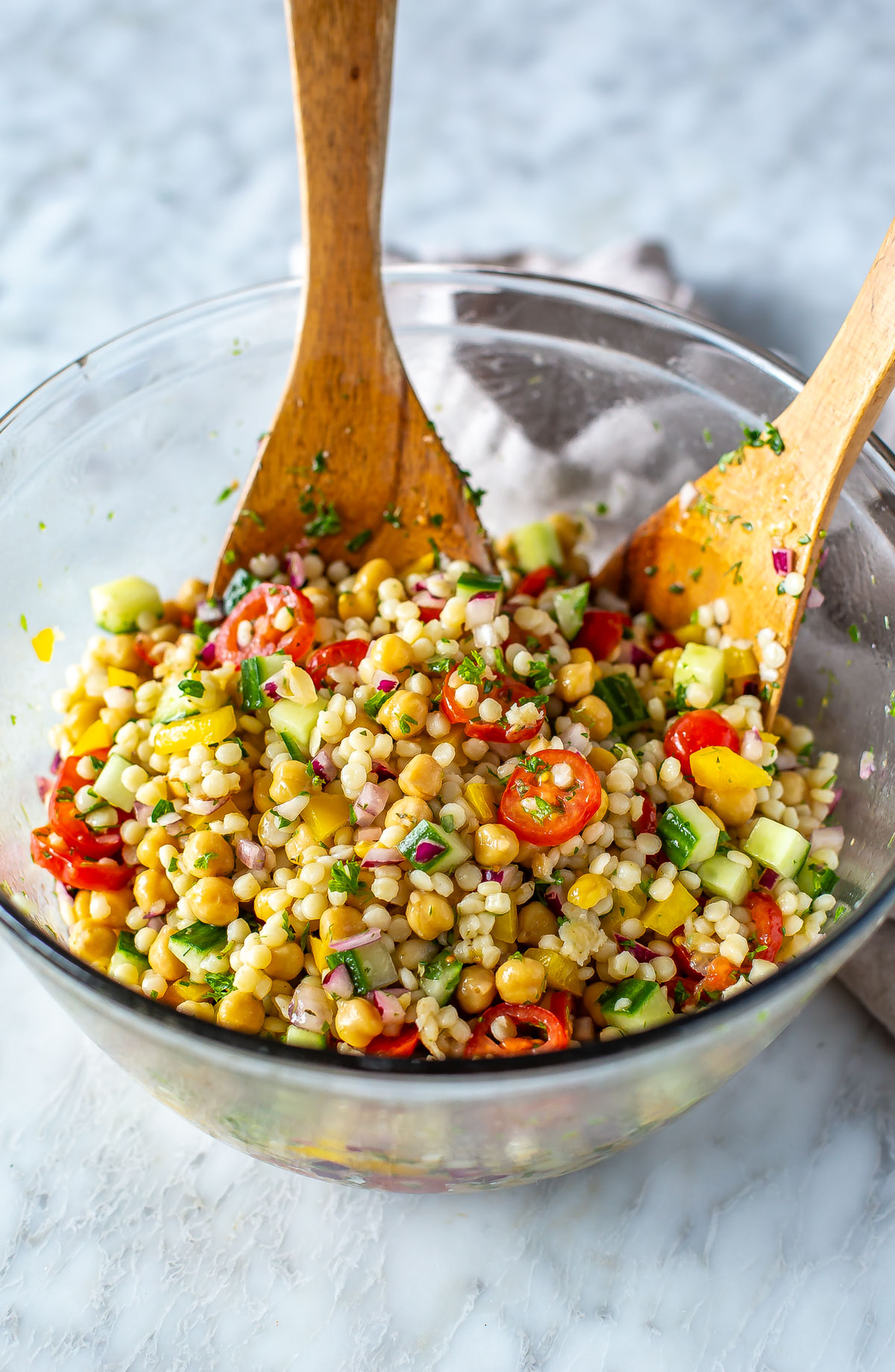 A big bowl of Mediterranean couscous salad with two large salad servers in it.