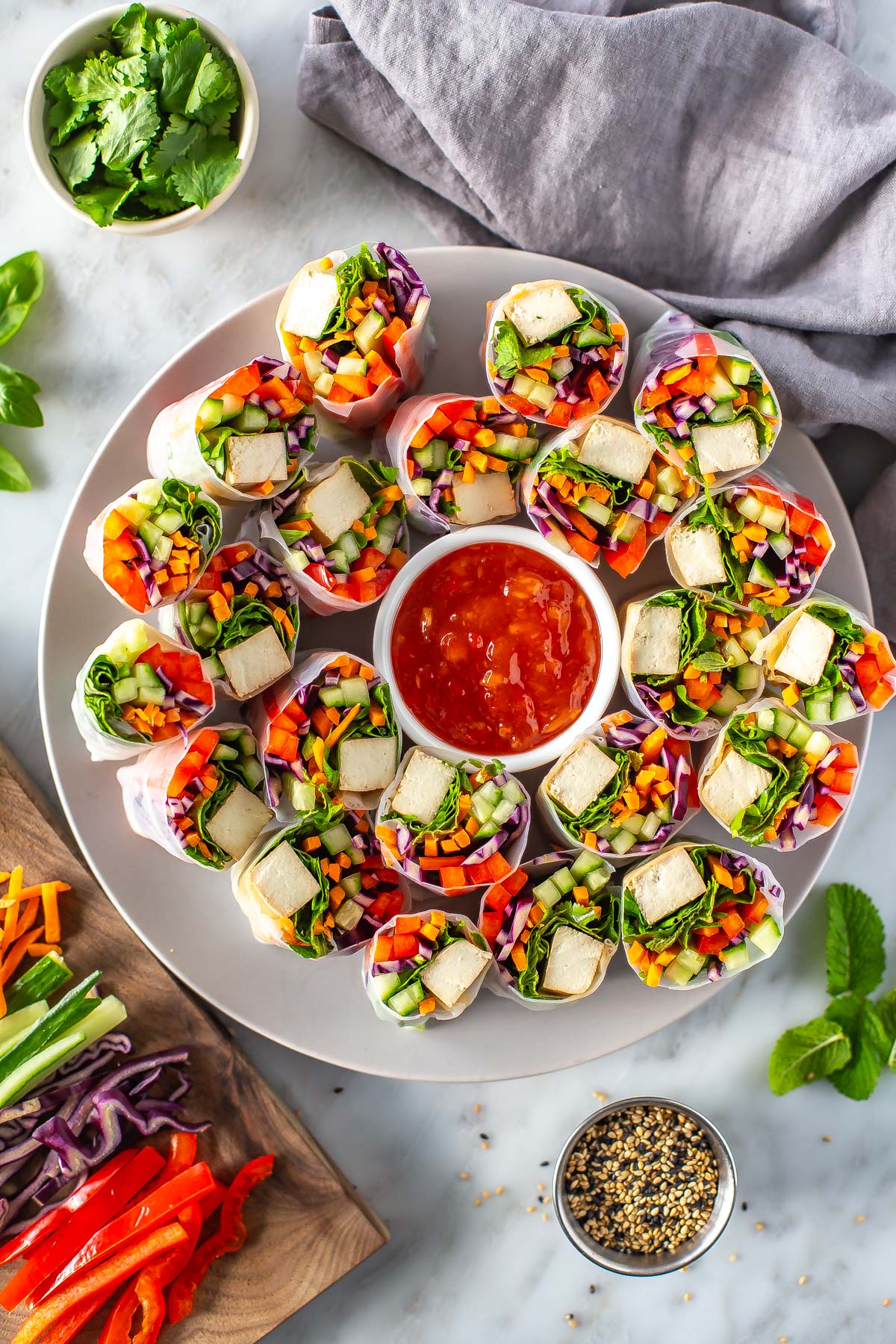 A large plate of summer rolls with a little bowl of sweet chili sauce in the middle.