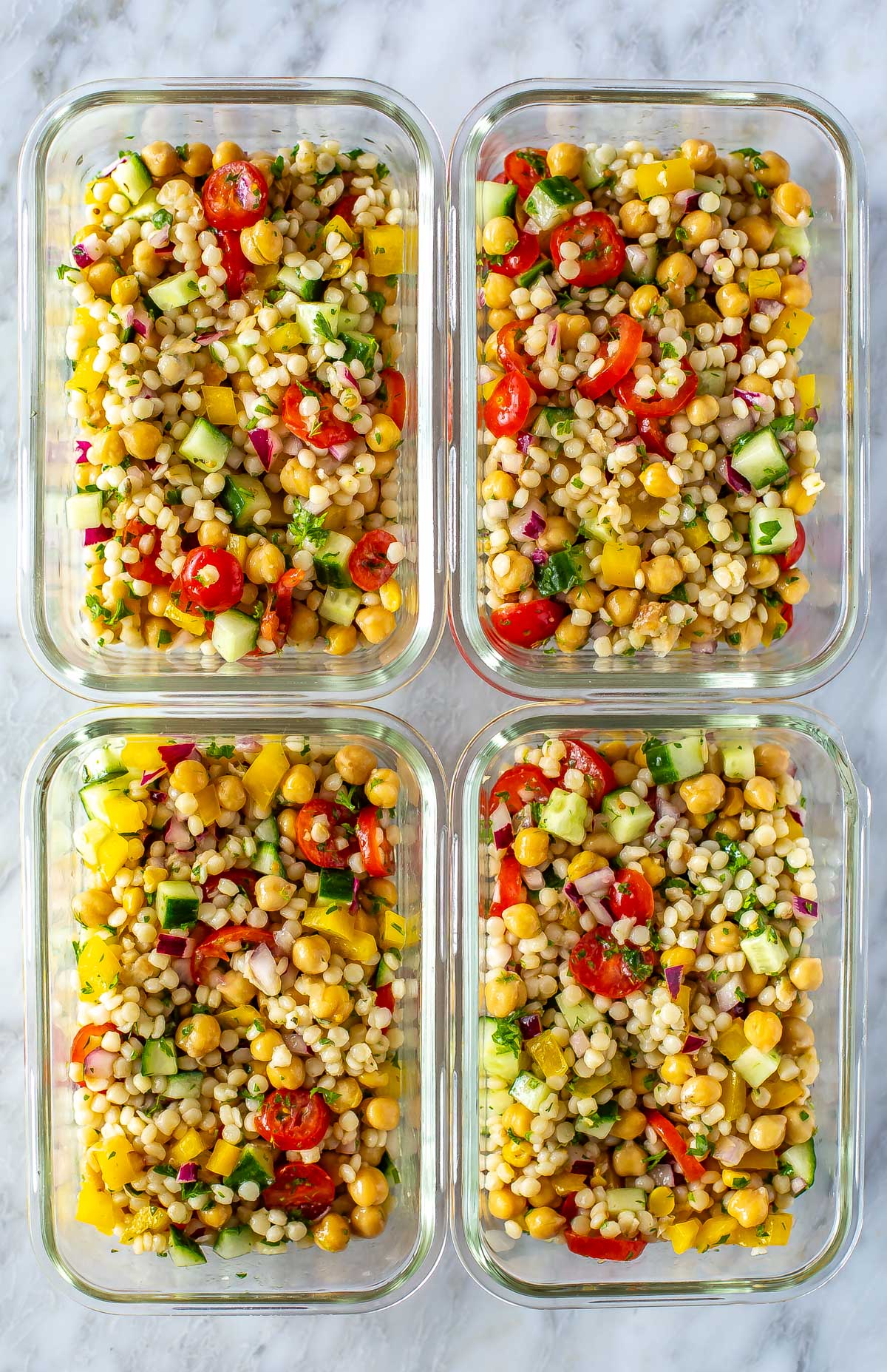 Four meal prep containers, each filled with a serving of Mediterranean couscous salad.