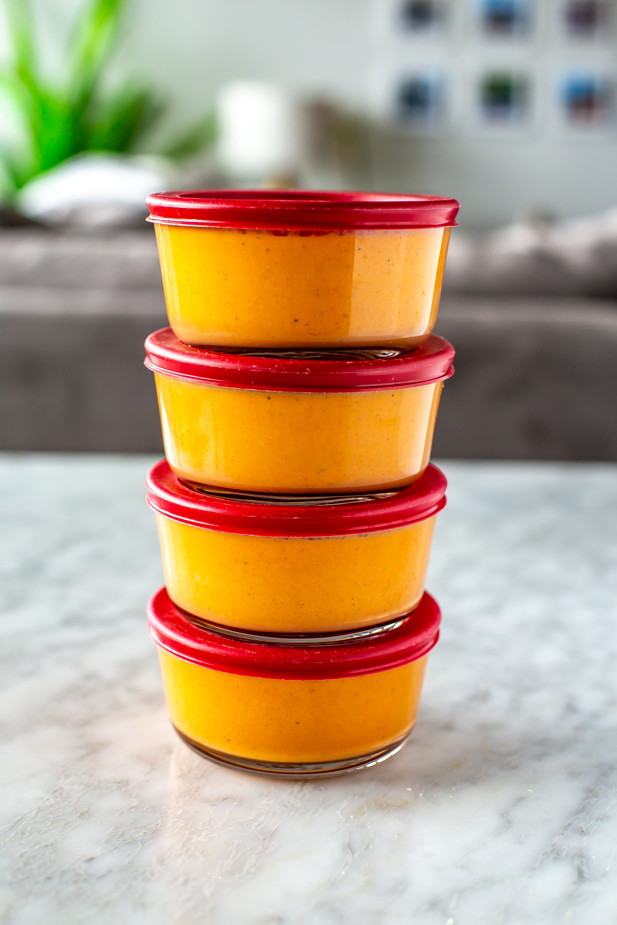 Four round glass meal prep containers stacked on top of each other, each with a serving of roasted tomato basil soup.