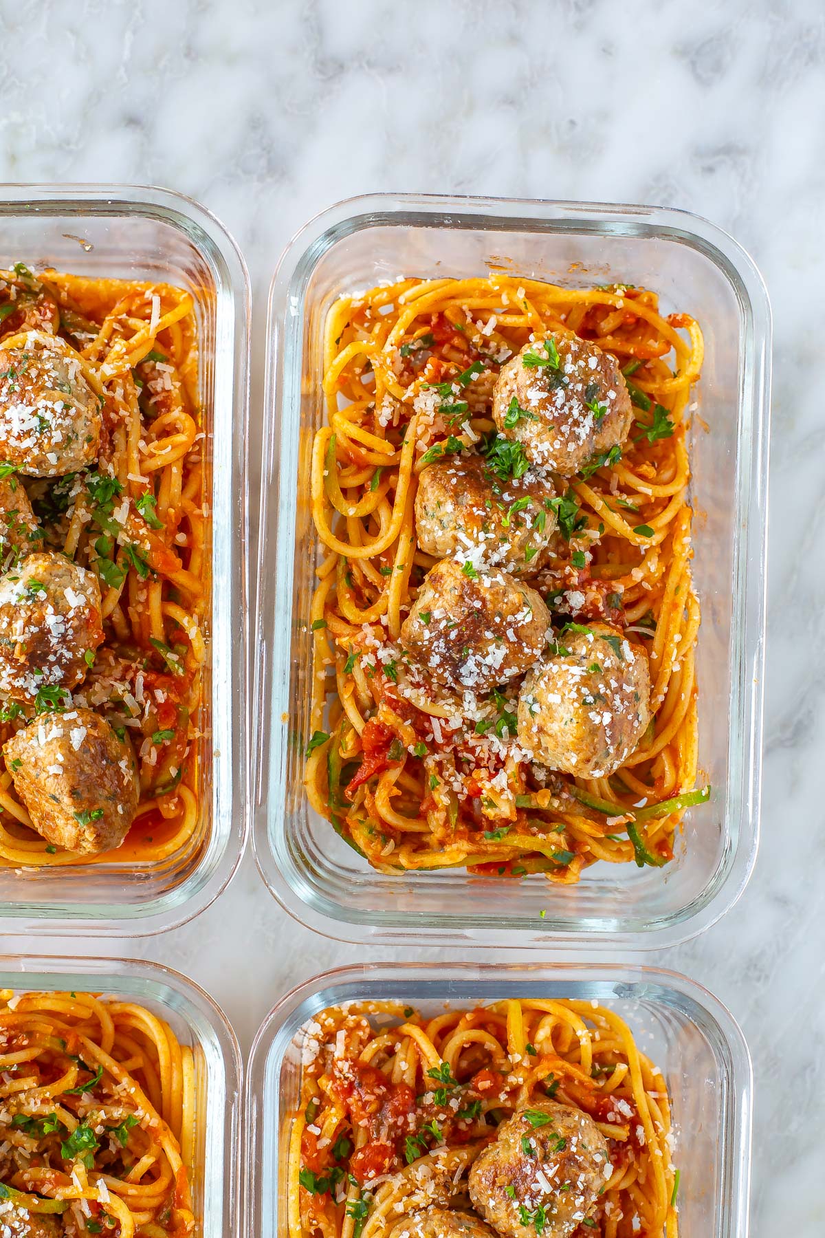 A close-up of baked turkey meatballs in a meal prep container with pasta and zucchini noodles.