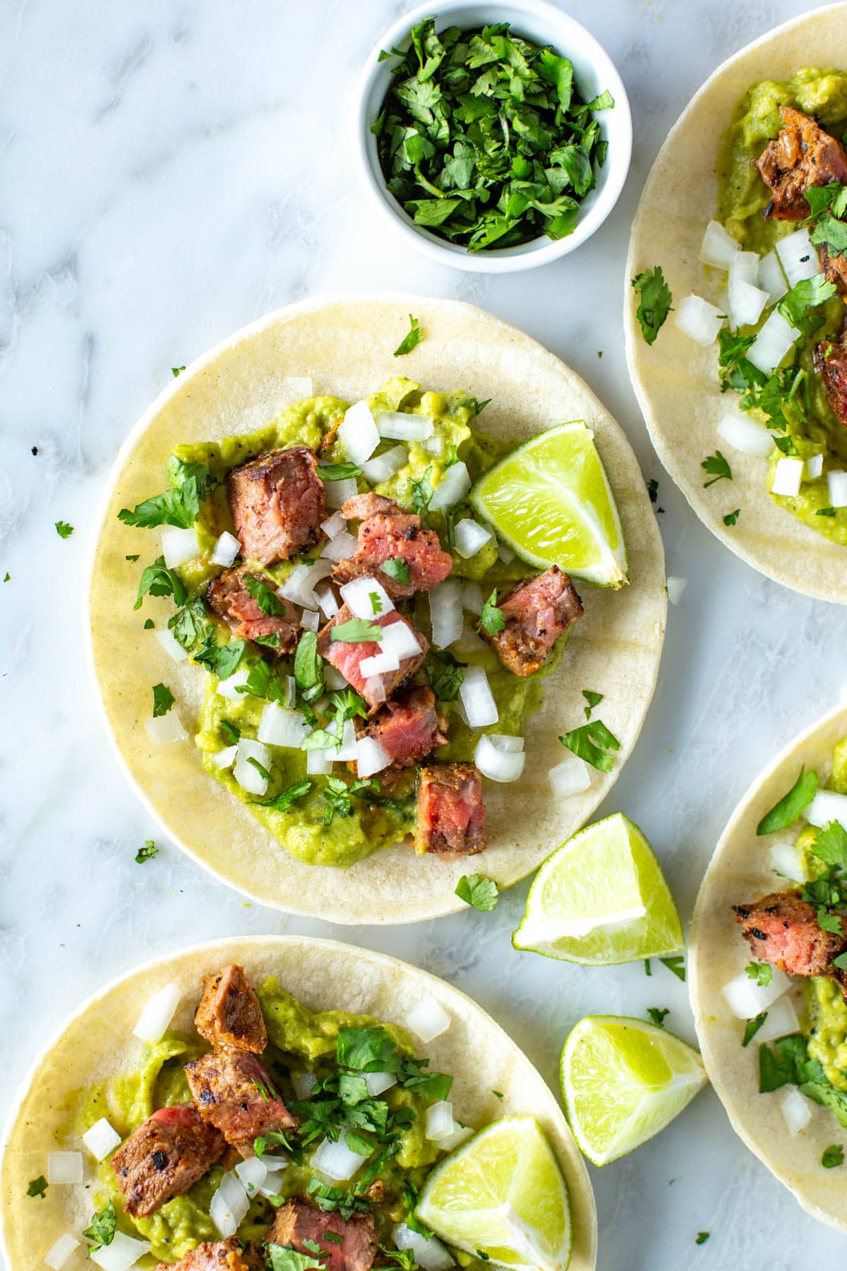 Close-up of assembled carne asada tacos with a side of chopped cilantro.