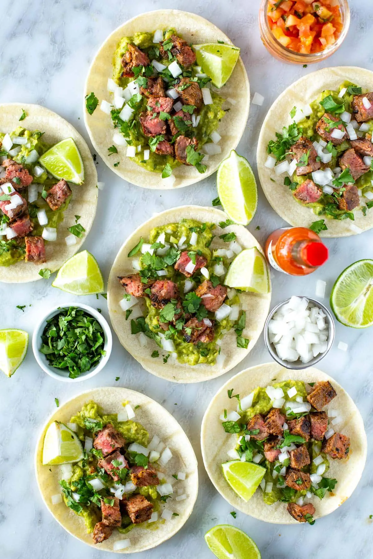 Assembled carne asada tacos garnishd with cilantro and lime wedges