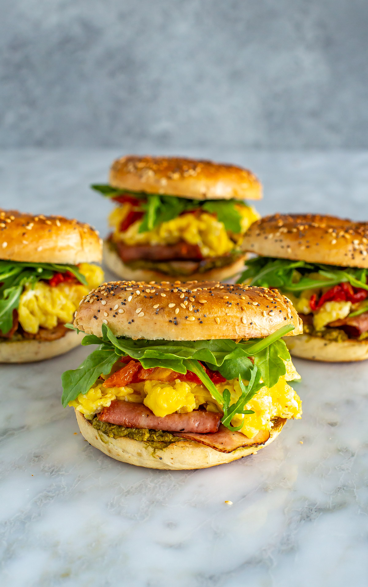 A close-up of four pesto breakfast bagel sandwiches.