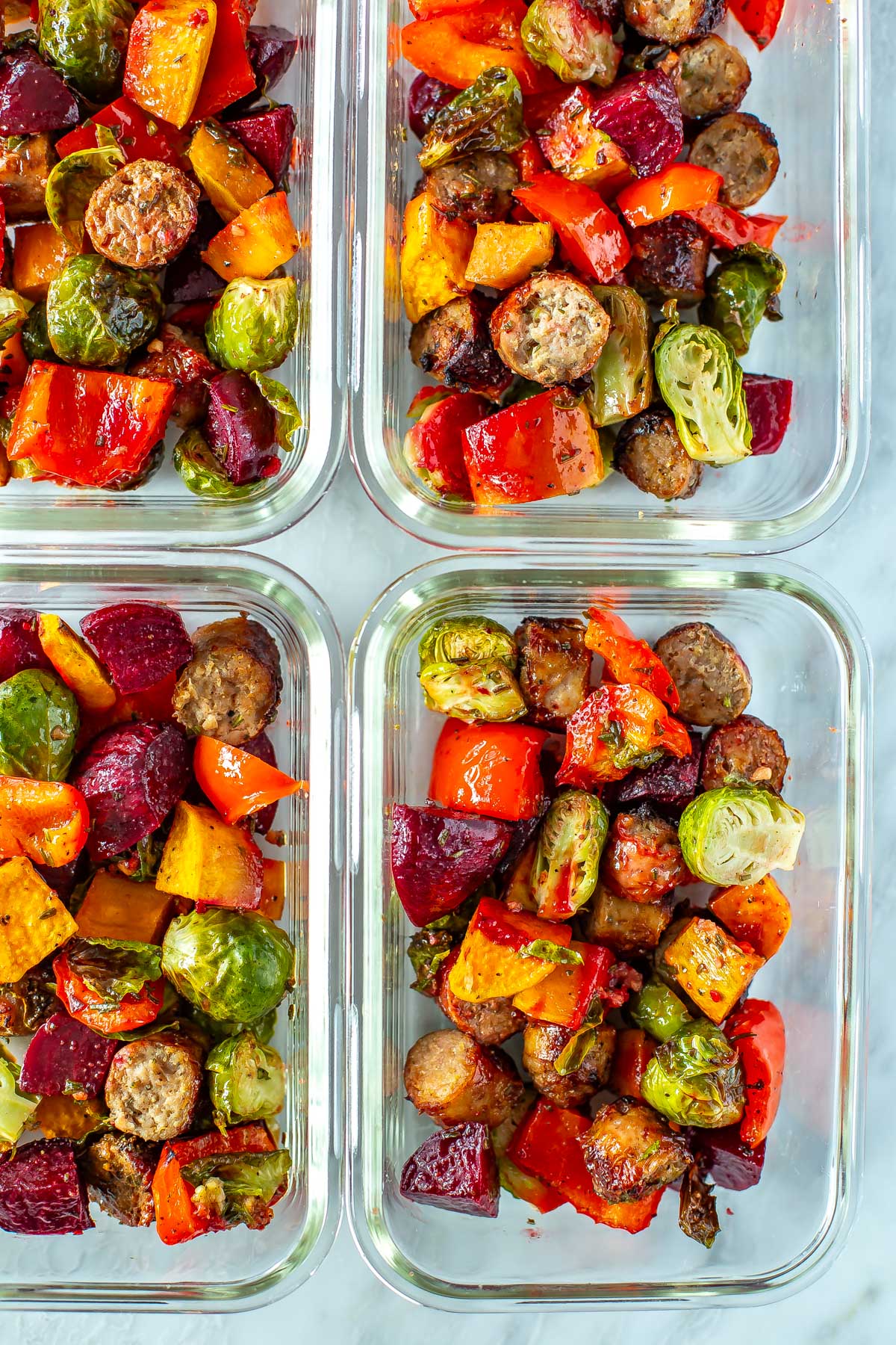 A close-up of sheet pan sausage and veggies in meal prep containers.