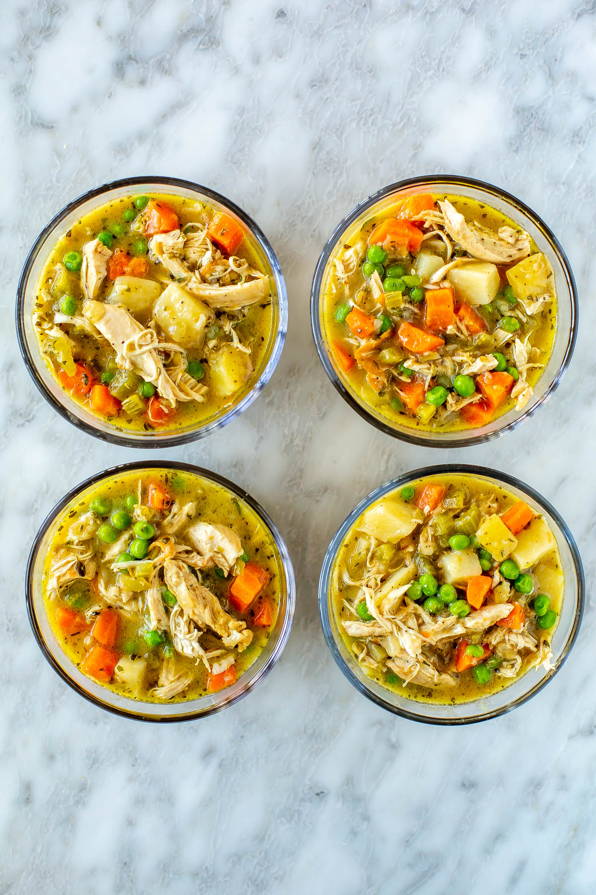 Four round meal prep containers, each with a serving of chicken pot pie soup.