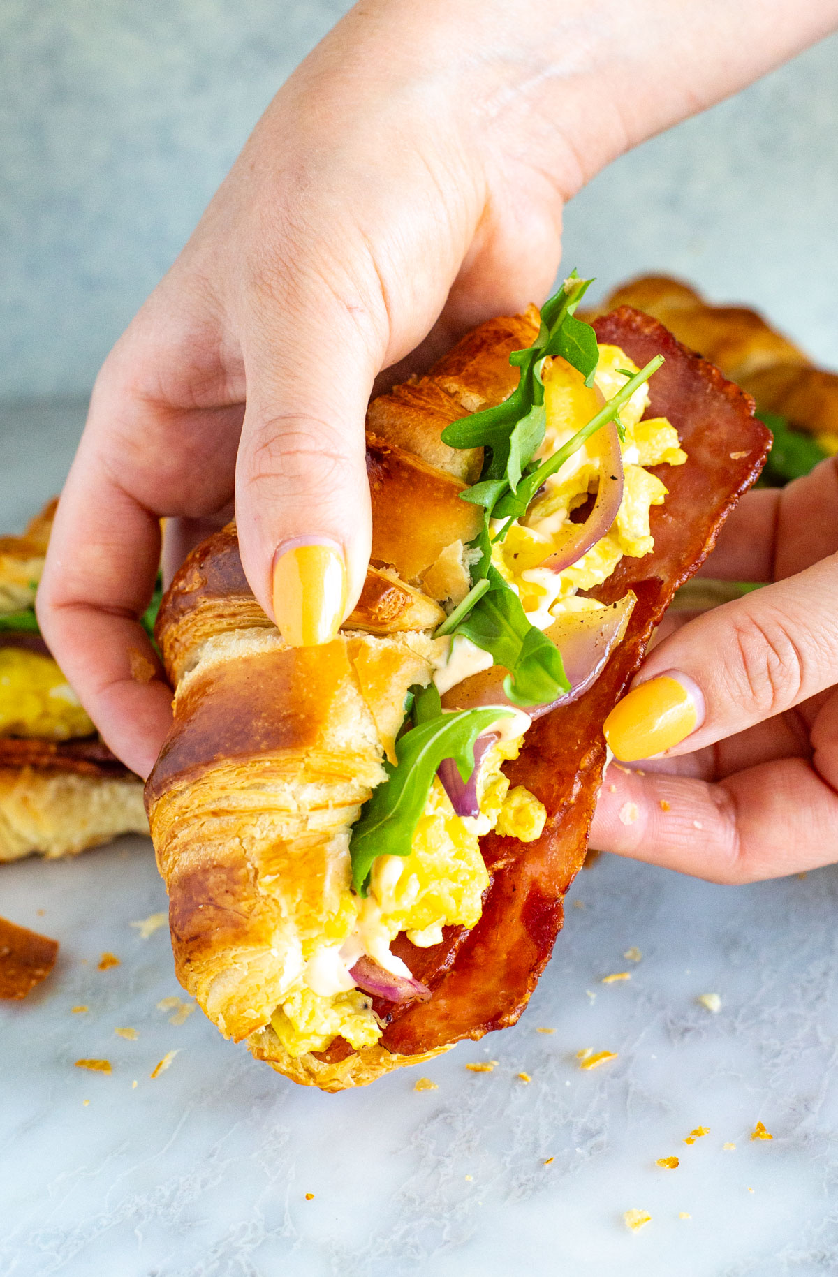 A hand holding a croissant breakfast sandwich.