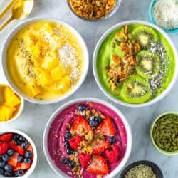 Three smoothie bowls with a variety of toppings.