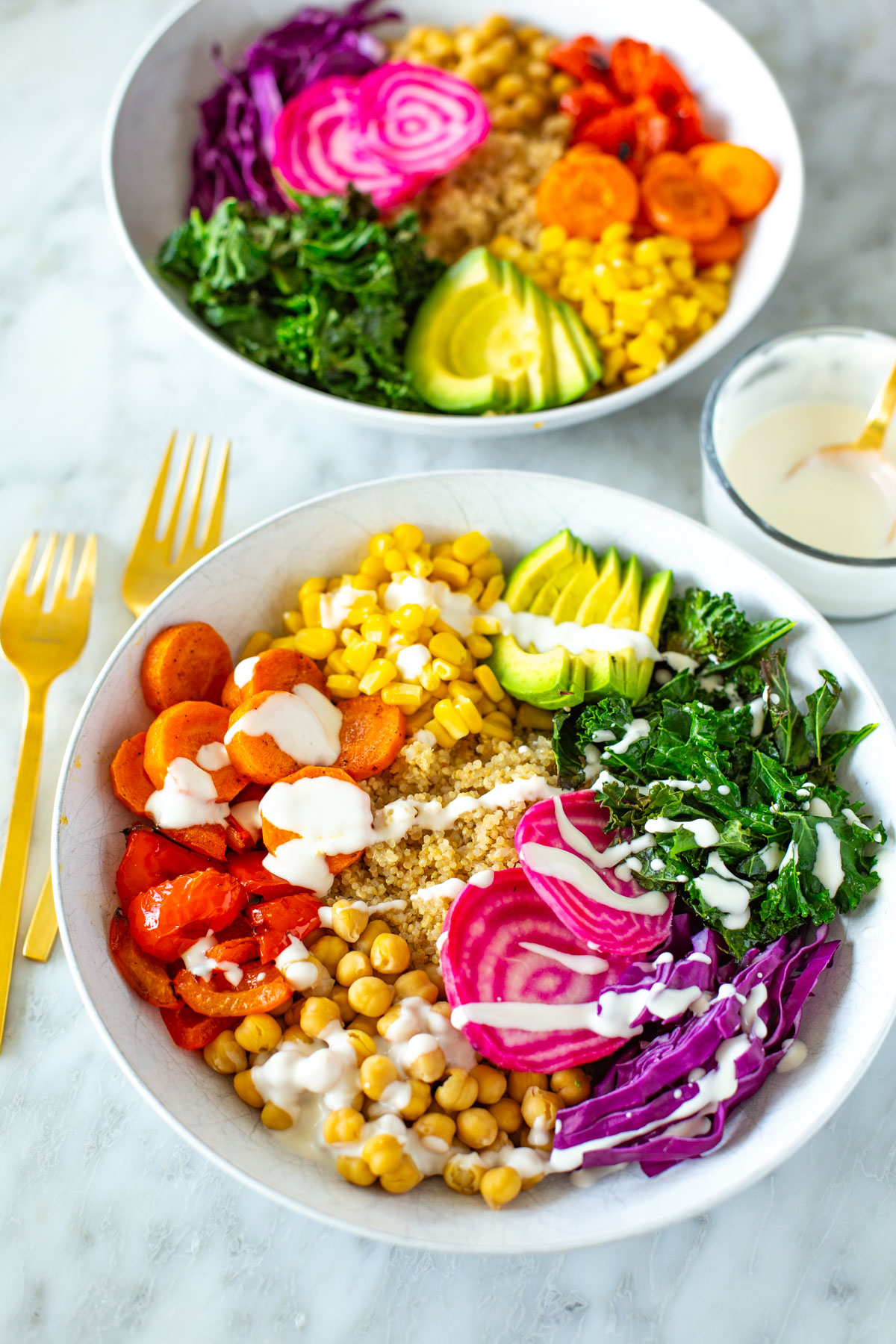 Two rainbow veggie bowls with garlic dressing drizzled over top.