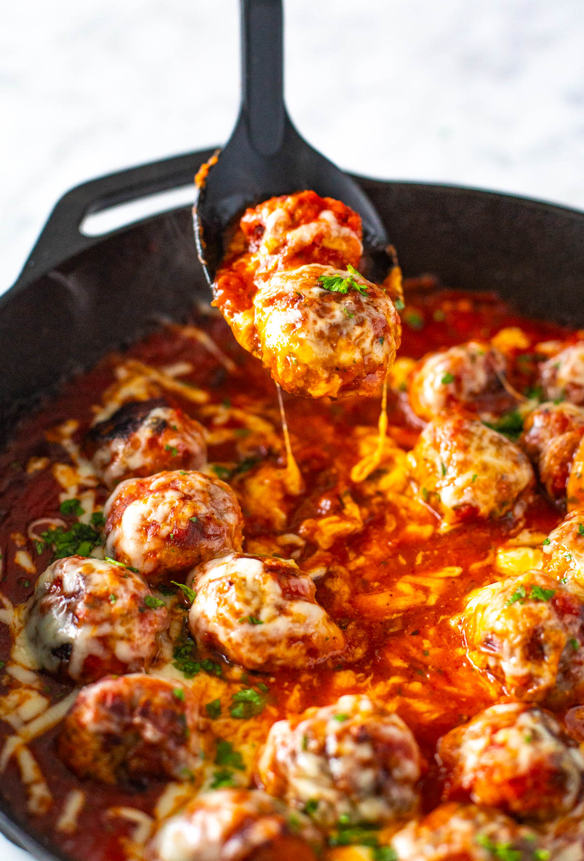A chicken parmesan meatball being picked up from a skillet.