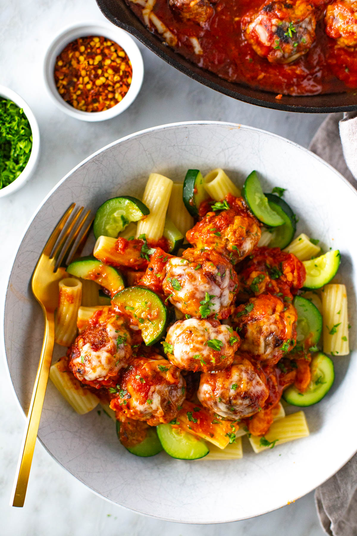 A close-up of chicken parmesan meatballs served alongside pasta and zucchini.