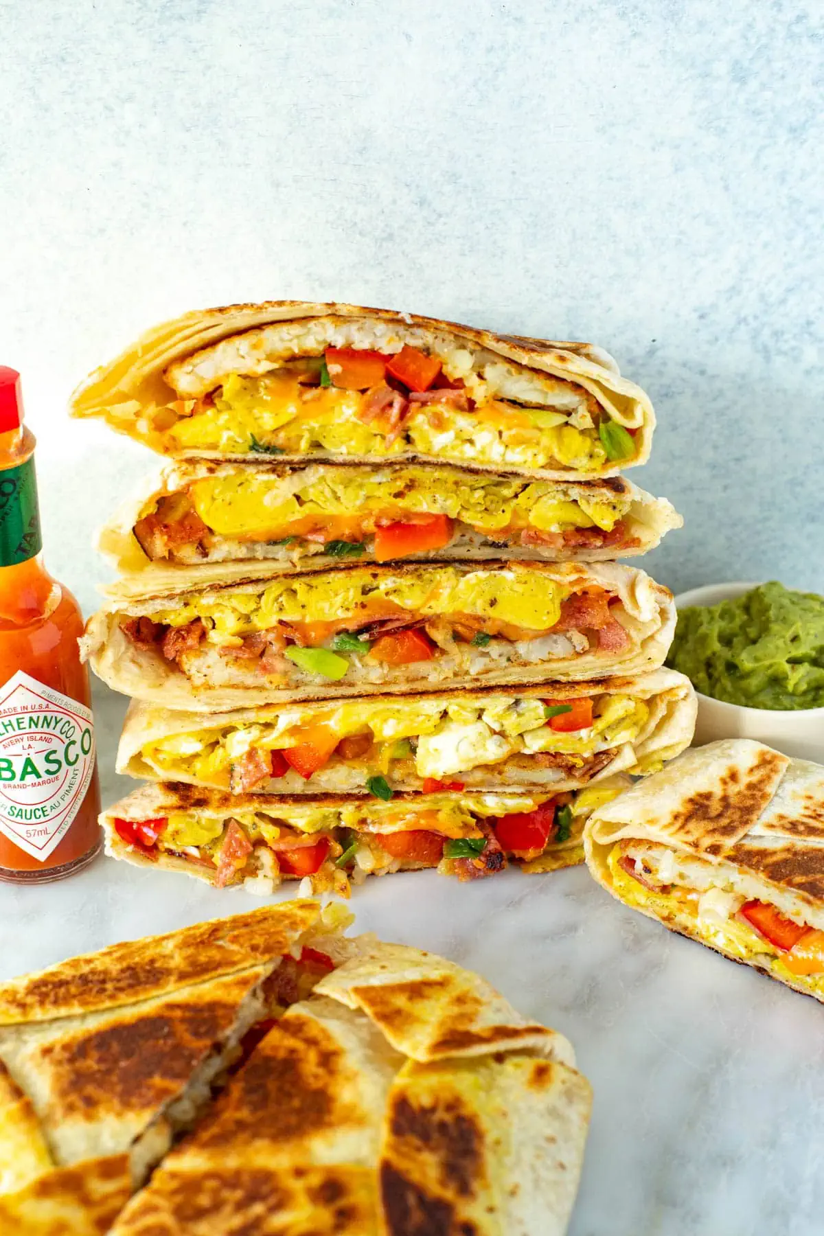Cut open breakfast crunchwraps stacked together with a side of hot sauce and guacamole