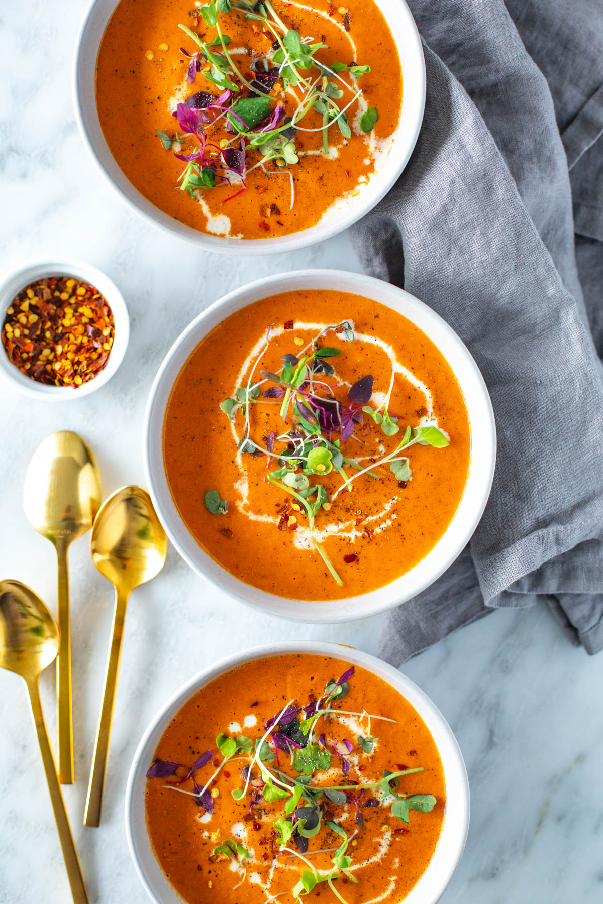 Bowls of roasted red pepper soup with gold spoons on the side