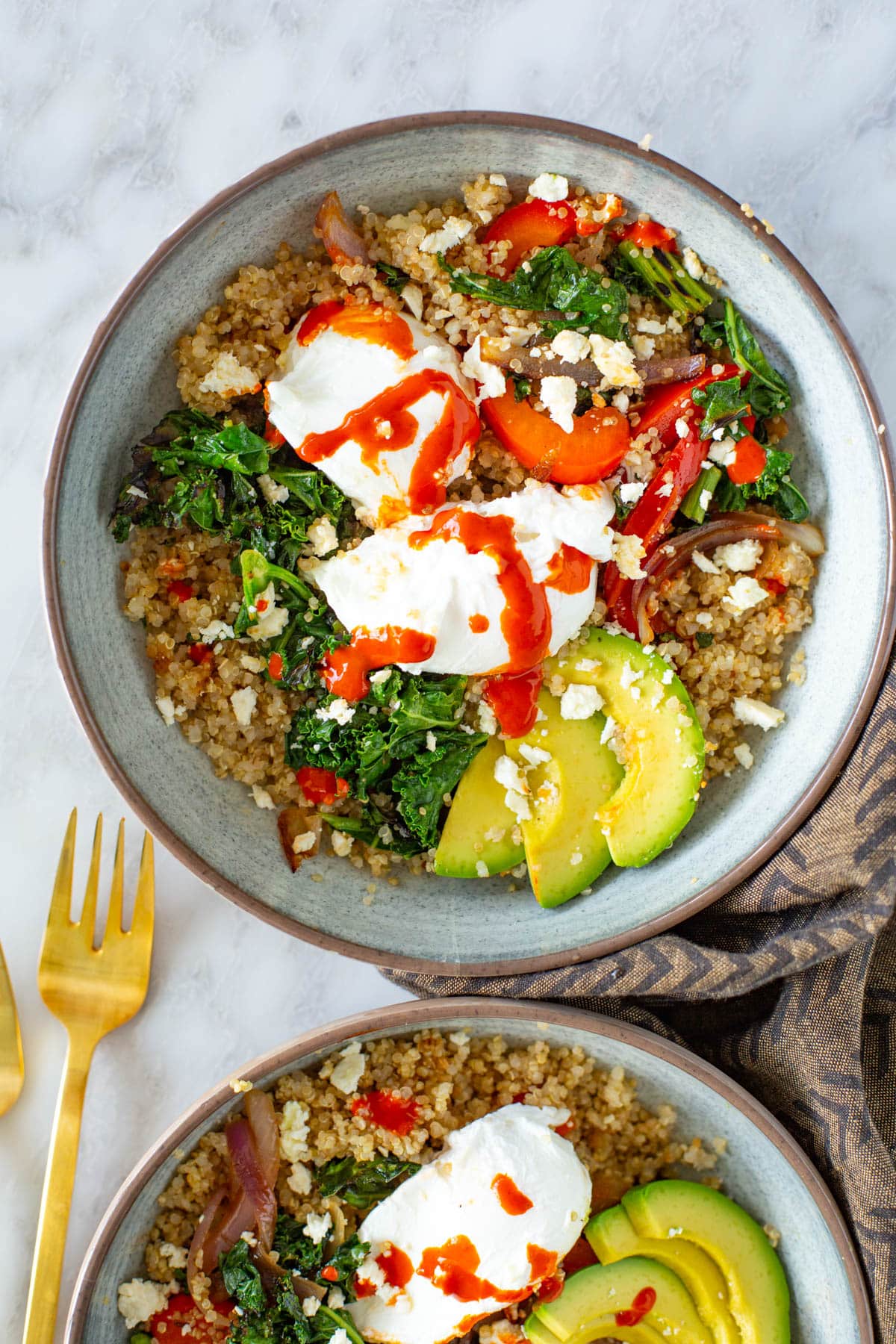 A close-up of a quinoa breakfast bowl with poached eggs, avocado and hot sauce.