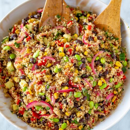 Overhead shot of quinoa salad with two wooden spoons tossing the salad