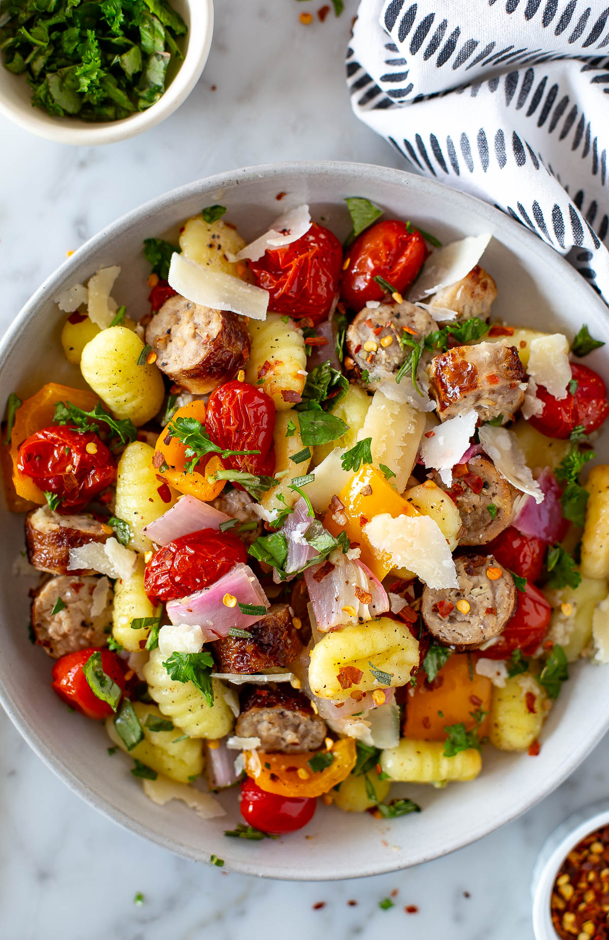 Plated sheet pan gnocchi with sausage, cherry tomatoes, and bell peppers, garnished with fresh herbs and parmesan cheese