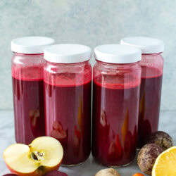 side shot of four jars of beet juice with white lids.