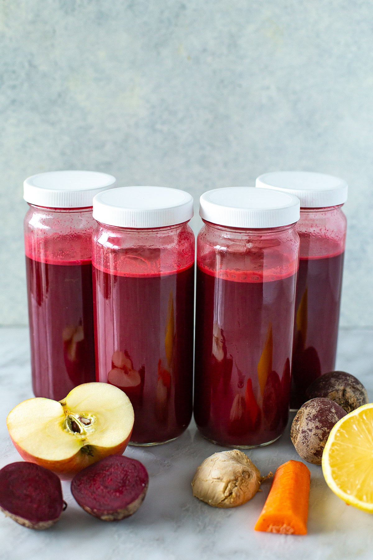 side shot of four jars of beet juice with white lids.