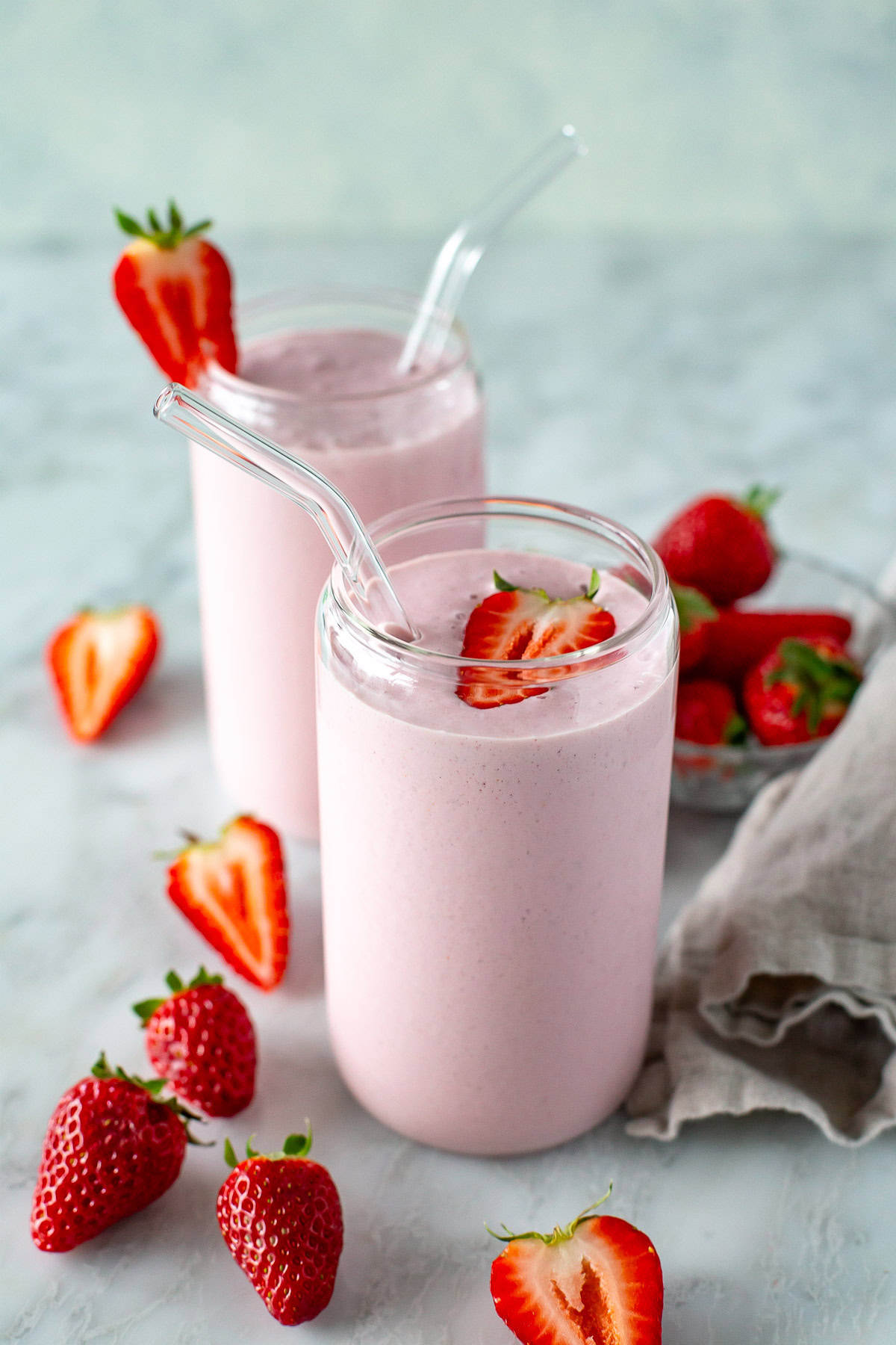 side shot of high protein strawberry smooth in 2 clear glasses and some strawberries around them 2