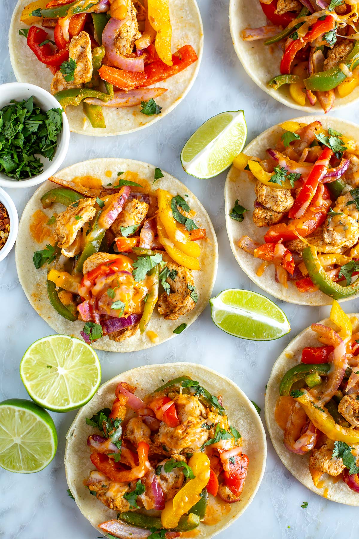 Overhead shot of an air fryer with cooked chicken fajita mixture, surrounded by tortillas filled with chicken, peppers, and onions, garnished with lime wedges 3