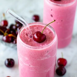 Side shot of a cherry smoothie with a fresh cherry on top and a straw.