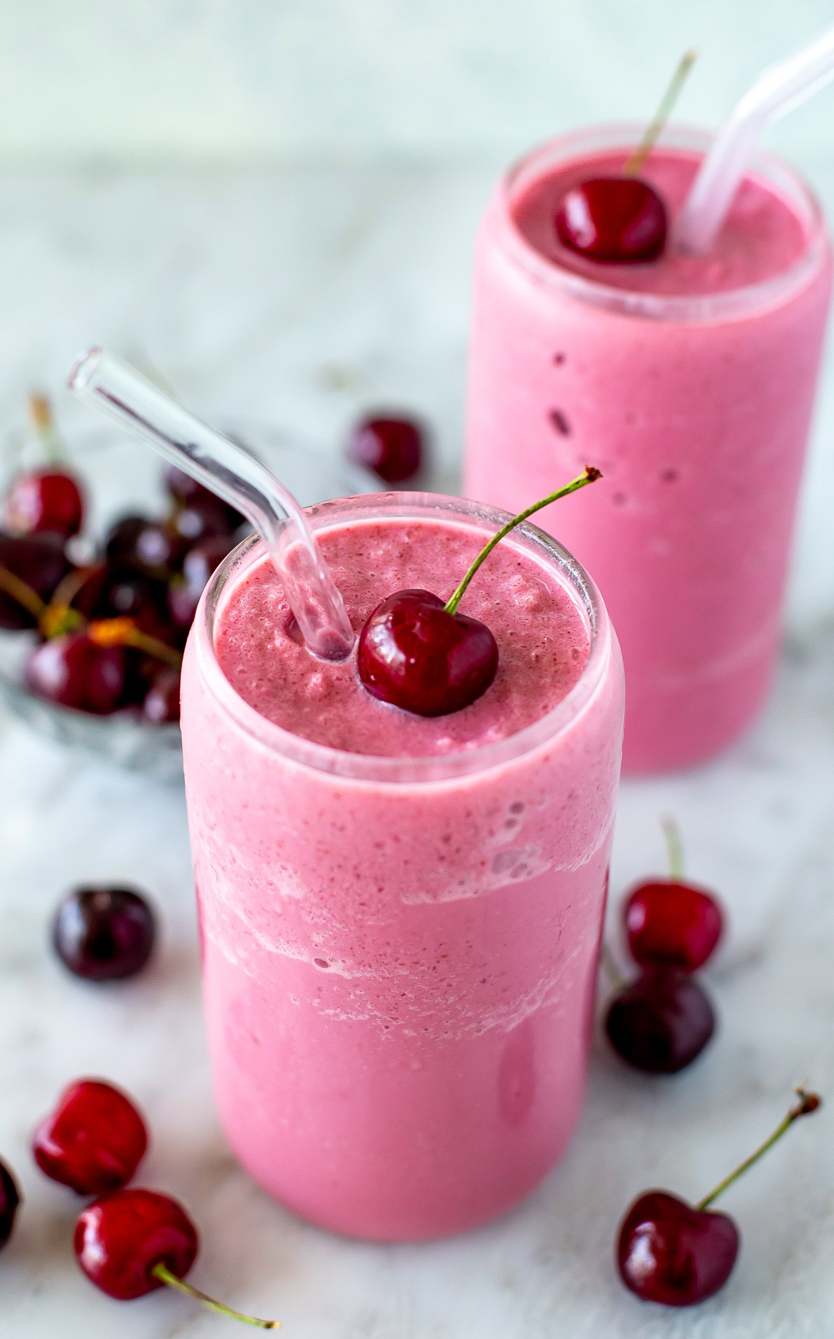 Side shot of a cherry smoothie with a fresh cherry on top and a straw.