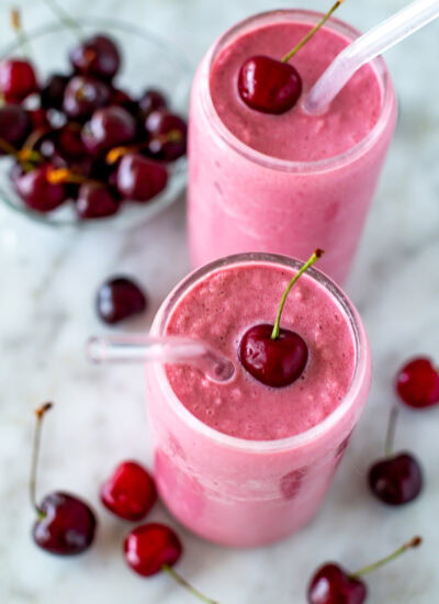 Overhead shot of two cherry smoothies with fresh cherries and straws.