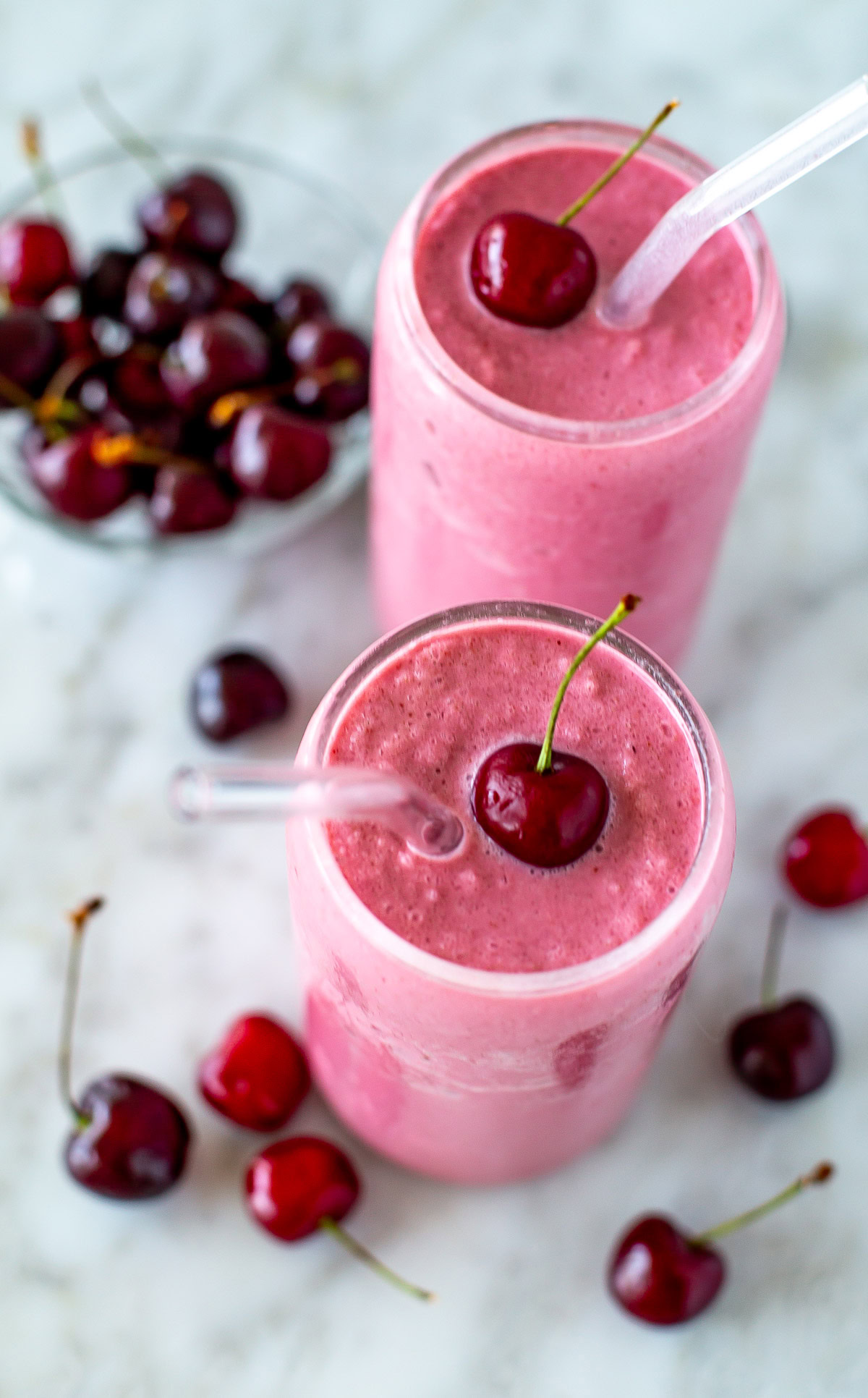 Overhead shot of two cherry smoothies with fresh cherries and straws.