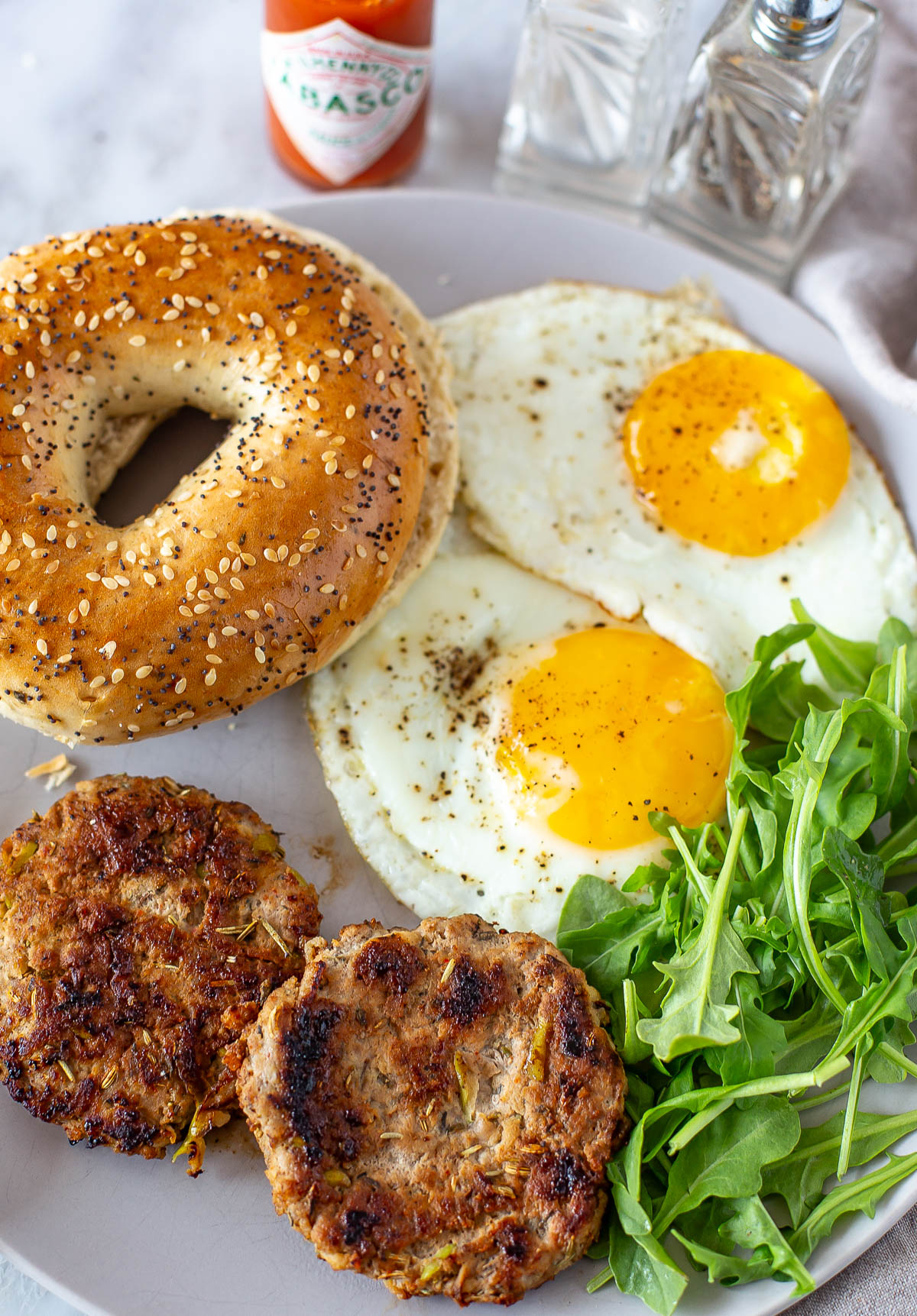 Overhead shot of two cooked chicken apple sausage patties, eggs, and a bagel.