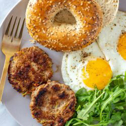 Overhead shot of a cooked chicken apple sausage patty on a plate with herbs and a lemon slice.