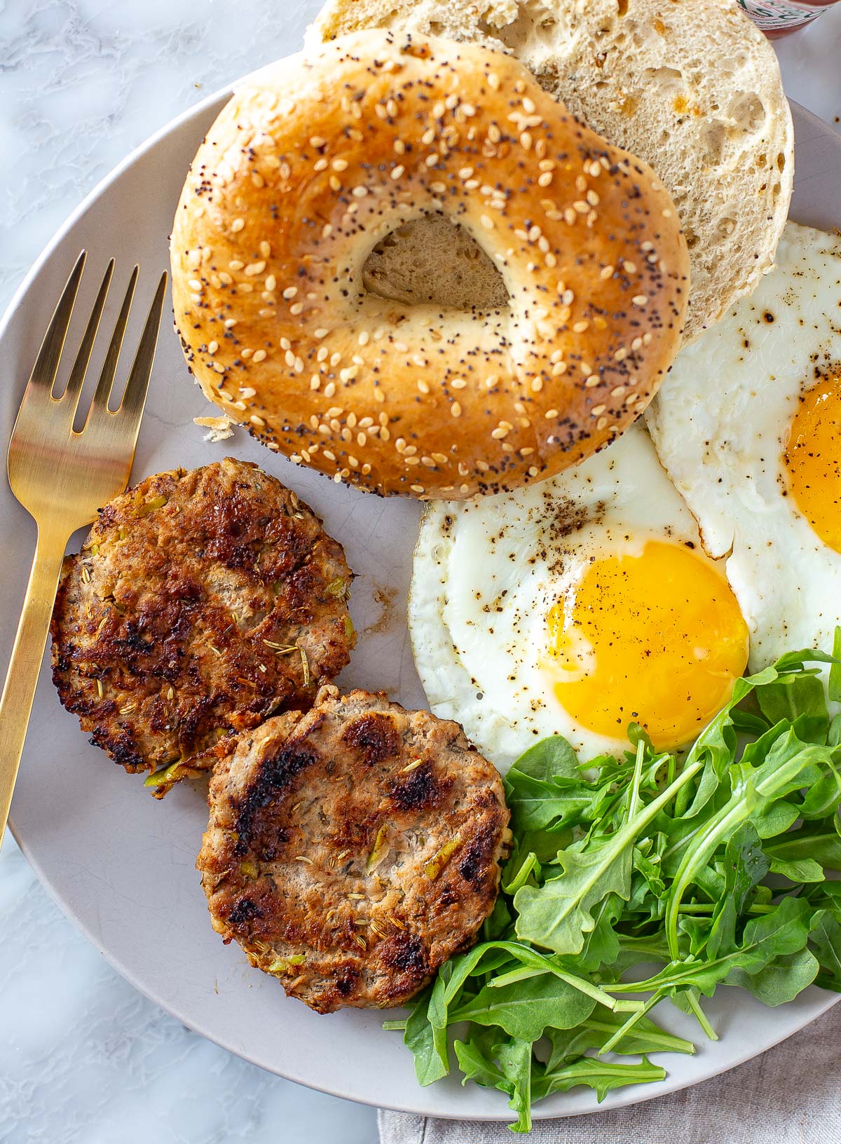 Overhead shot of a cooked chicken apple sausage patty on a plate with herbs and a lemon slice.