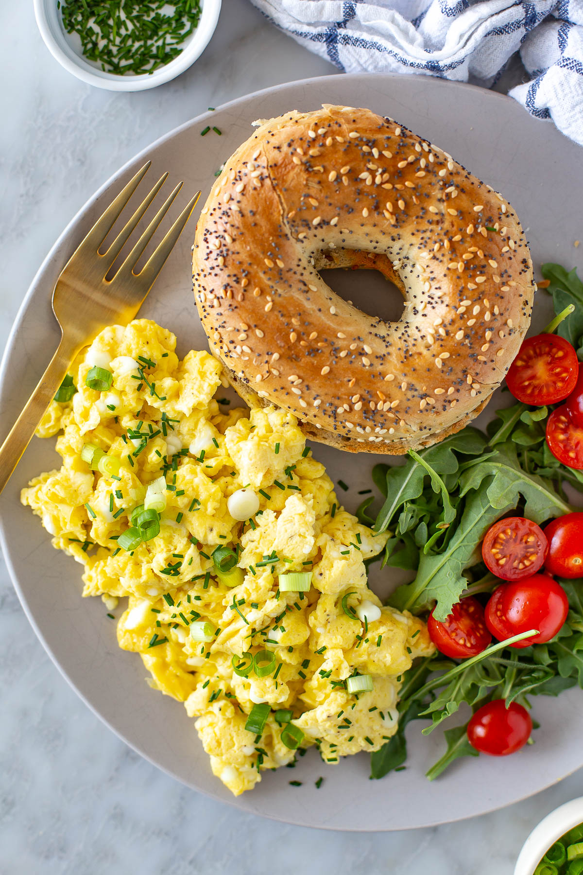 Overhead shot of cottage cheese eggs with a bagel, a side of arugula, and tomatoes.