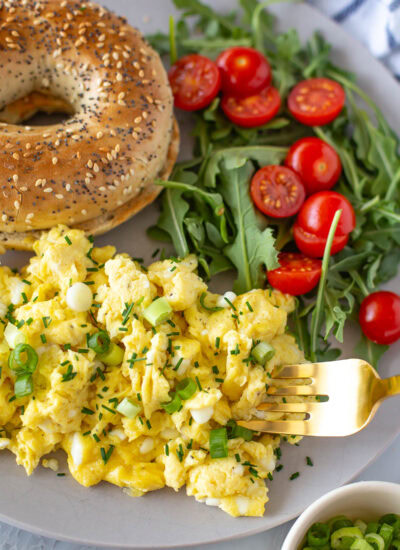 Overhead shot of a plate of cottage cheese eggs with a bagel and arugula salad.