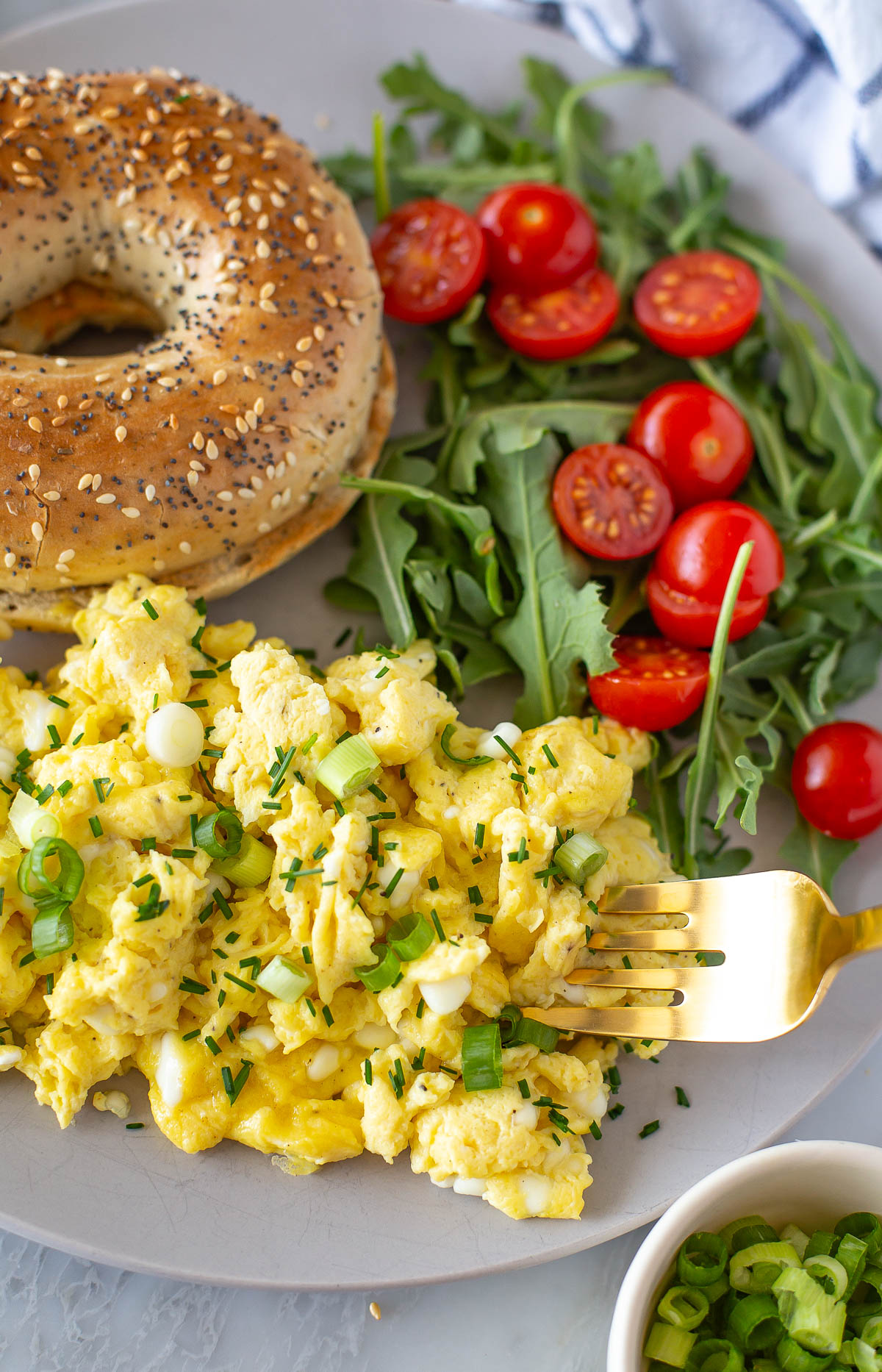 Overhead shot of a plate of cottage cheese eggs with a bagel and arugula salad.