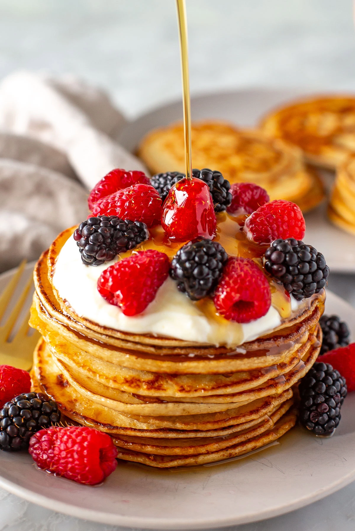 Side shot of syrup being drizzled onto a stack of pancakes with berries.